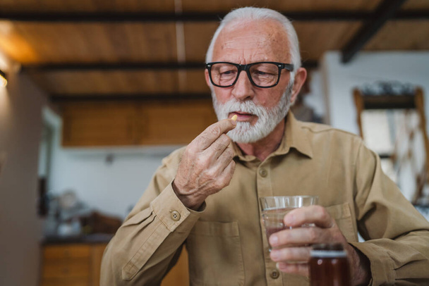 Een oudere man Kaukasische mannelijke grootvader zitten thuis te nemen drug tablet drinken pijnstillers of vitamine supplement lees label geneeskunde echte persoon gezondheid en geneeskunde concept kopiëren ruimte - Foto, afbeelding