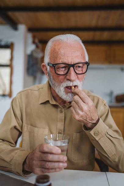 Jeden senior mężczyzna kaukaski mężczyzna dziadek siedzieć w domu wziąć tabletki leków przeciwbólowych lub witaminy suplement czytać etykiety medycyny prawdziwe osoby zdrowia i medycyny pojęcie przestrzeni kopii - Zdjęcie, obraz
