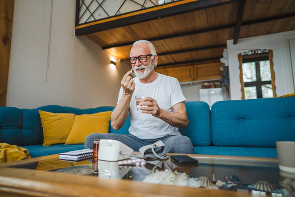 Egy idős férfi kaukázusi férfi nagyapa ül otthon vegye kábítószer tabletta ital fájdalomcsillapítók vagy vitamin kiegészítés olvasni címke orvostudomány valós személy egészség és orvostudomány koncepció másolás tér - Fotó, kép