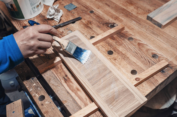 Σκαρφαλώνοντας ένα ξύλινο συρτάρι, εργαστήριο ξυλουργικής. Το βερνίκι εφαρμόζεται σε μια ξύλινη σανίδα με ένα πινέλο - Φωτογραφία, εικόνα