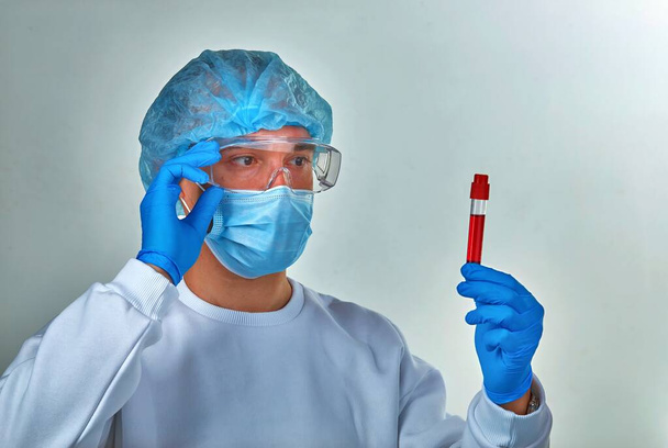Lékař v masce při pohledu na krevní zkumavku na koronavirus COVID19, HIV, ebolu nebo jinou nebezpečnou infekci. Lékařské zázemí, nástroje, šablony, tapety. Koncept koronavirové choroby - Fotografie, Obrázek