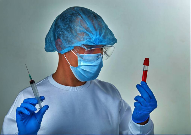 Médecin masqué effectuant le test sanguin pour le coronavirus COVID19, le VIH, le virus Ebola ou toute autre infection dangereuse. Fond médical, instruments, modèle, papier peint. Concept de maladie à coronavirus. Portrait de docteur
 - Photo, image