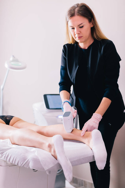Mujer recibiendo un procedimiento de depilación láser en su pierna por un esteticista profesional en un salón de belleza. - Foto, imagen