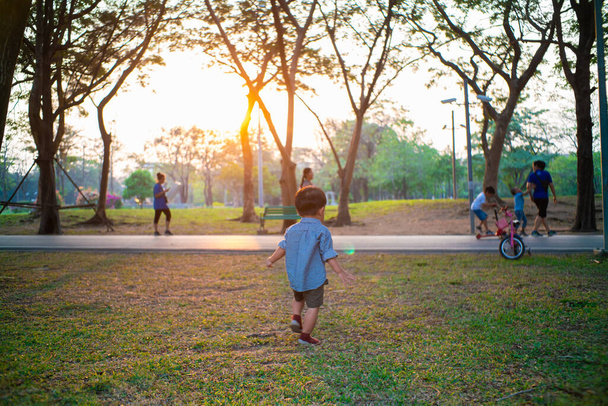 Ευτυχισμένο χαρούμενο παιδί ασιατικό 2 ετών αγόρι παίζει στην πόλη δημόσιο πάρκο ηλιοβασίλεμα ζεστό φως υπαίθρια δραστηριότητα - Φωτογραφία, εικόνα