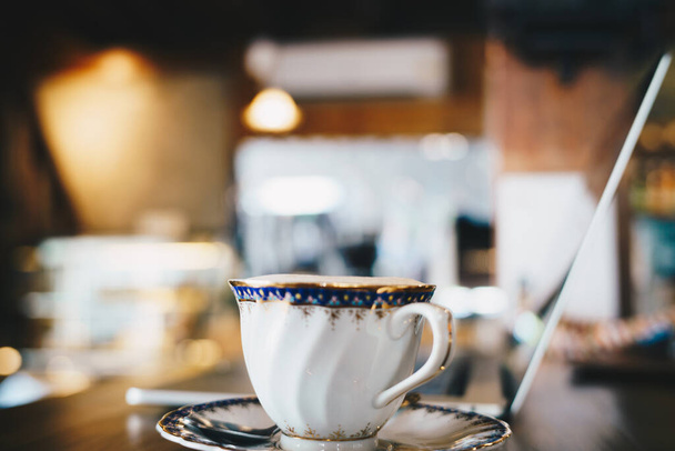 taza de café vintage blanco con vista lateral portátil en escritorio de madera   - Foto, Imagen