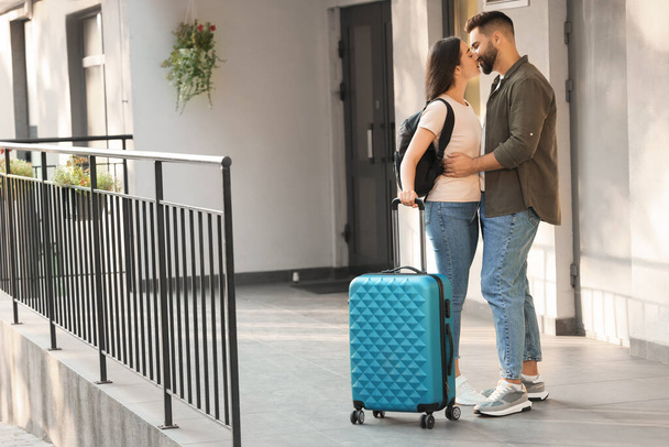 Long-distance relationship. Beautiful young couple with luggage kissing near house entrance outdoors - Fotografie, Obrázek