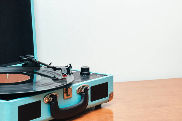 Poziome zdjęcie gramofonu w kształcie niebieskiej walizki, na drewnianym stole i białym tle. Pojęcie hobby, sztuka. - Zdjęcie, obraz
