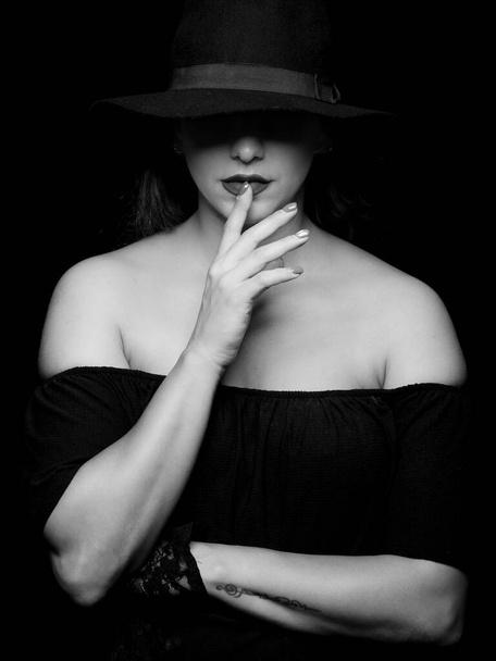 Portrait d'une jeune femme caucasienne portant un chapeau avec la main sur les lèvres. Coup de tête noir et blanc d'une jolie fille - Photo, image