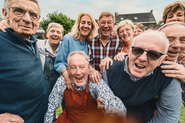 Żywa grupa seniorów zostaje złapana w szczerym momencie czystej radości i śmiechu. Zebrani na zewnątrz, ich prawdziwe uśmiechy i ciasna więź promieniują ciepłem i pięknem przyjaźni na całe życie.. - Zdjęcie, obraz