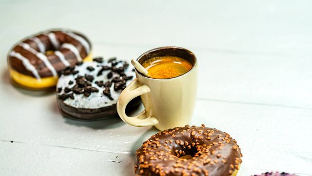 Coloridos donuts y taza de café en la mesa de madera blanca. Pastelería dulce con aspersiones acristaladas, concepto de desayuno. Vista superior con espacio de copia - Foto, imagen