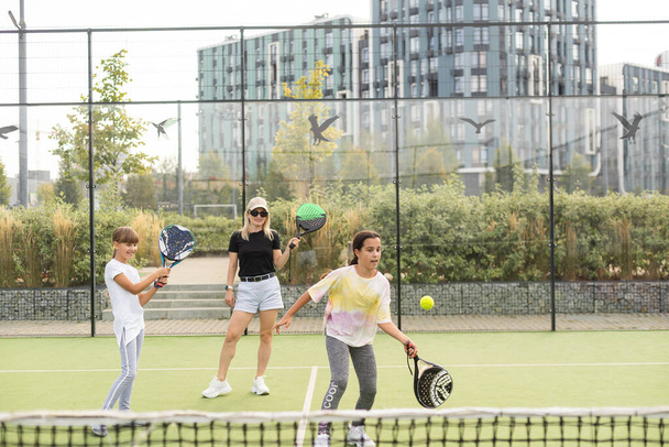 Veselý trenér učí dítě hrát tenis, zatímco oba stojí na tenisovém kurtu. Kvalitní fotografie - Fotografie, Obrázek