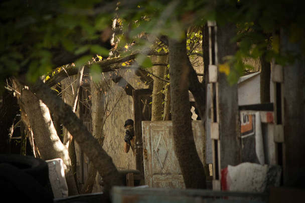 Onder de schuilplaatsen op een zonnige dag is er een man met een wapen, een airsoft speeltuin - Foto, afbeelding