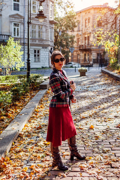 Full body portret van stijlvolle modieuze vrouw dragen blazer rok laarzen wandelen in de herfst park tussen bladeren met portemonnee. Herfstkleding - Foto, afbeelding