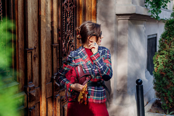 Портрет стильної жінки, що носить застібку-кіготь для волосся, що тримає червоний гаманець у картатому блістері, аксесуари на осінній вулиці міста. Падіння модного старого грошового вбрання - Фото, зображення