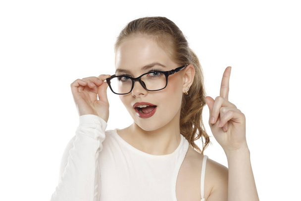 Ritratto di bella donna bionda positiva che indossa gli occhiali e punta su uno sfondo bianco da studio - Foto, immagini