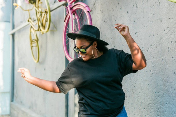 afroamericana femminile che ascolta musica in cuffia e balla allegramente per strada divertendosi - Foto, immagini