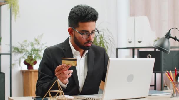 Arap iş adamı programcı yazılım geliştirici kredi kartı ile online satın alma alışverişi yapıyor ve ev ofis masasında dizüstü bilgisayar kullanıyor. Hintli serbest çalışan iş adamı - Video, Çekim