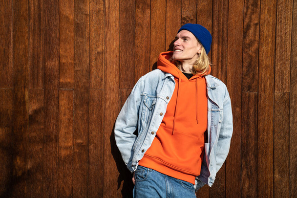 Smiling blond long hair guy scandinavian androgynous appearance standing near wooden fence looking aside. LGBT gay transgender bisexual man enjoying nature. Individuality personality minority concept. - Photo, Image