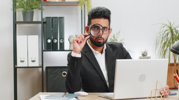 Investigator researcher scientist businessman working at home office holding magnifying glass near face looking into camera with big zoomed funny eye, searching, analyzing. Professional freelancer man - Footage, Video