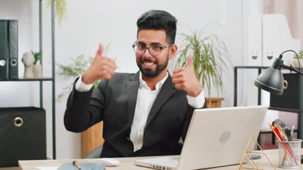 Comme ça. Heureux jeune homme d'affaires indien qui travaille sur un ordinateur portable en regardant avec approbation la caméra montrant pouces vers le haut, comme signe positif quelque chose de bon, rétroaction positive sur le lieu de travail de bureau. Homme indépendant - Séquence, vidéo