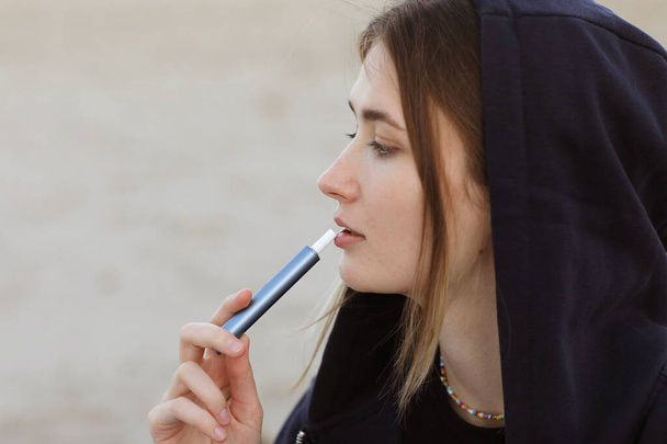 Tecnología de cigarrillos electrónicos. Mujer joven fuma y libera vapor de dispositivo de cigarrillo híbrido que utiliza recambios de tabaco reales con una almohadilla de calefacción, sistema de calefacción de tabaco. Malo hábito no saludable. - Foto, Imagen
