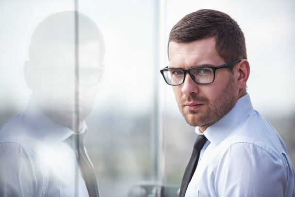 Portrét pohledný podnikatel v brýlích při pohledu na fotoaparát při stání v budově úřadu - Fotografie, Obrázek