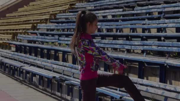 Młoda dziewczyna robi ćwiczenia gimnastyki na stadionie. Rozciągający się na nogi i stopy przed wyścigiem. - Materiał filmowy, wideo