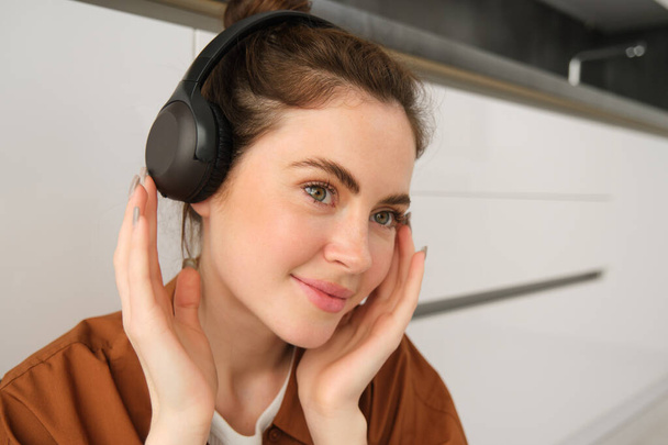 Imagen de la mujer moderna, hermosa chica disfruta escuchando música, tiene auriculares inalámbricos negros, se sienta en el suelo y descansa. - Foto, Imagen