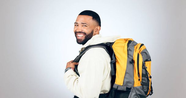 Man, happy portrait and hiking in studio with backpack and smile from travel and freedom with adventure. Camping, fitness and grey background and walking with trekking gear for vacation and holiday. - Photo, Image