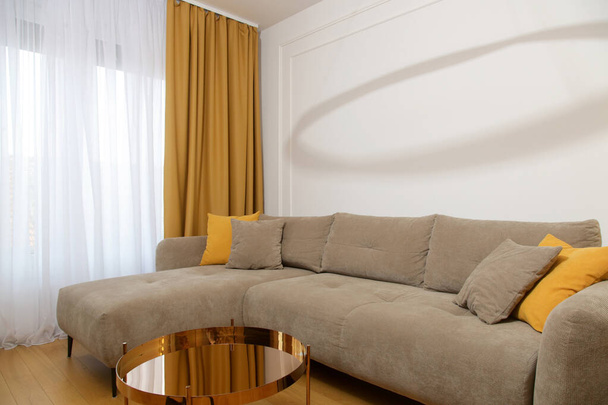 Comodo divano grigio con cuscino giallo senape, tende e tavolino, moderno concetto di soggiorno.  - Foto, immagini