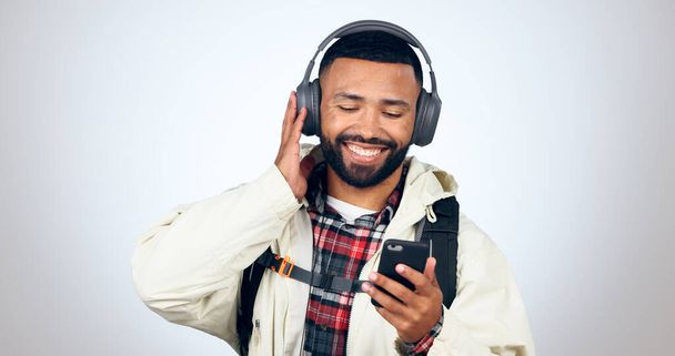 Man, Reisen und Hören mit Kopfhörer und Telefon für Musik im Studio, weißen Hintergrund oder Audio-Streaming. Radio, Podcast oder Person wandern und entspannen mit Hip-Hop-Sound, App-Download oder Technologie. - Foto, Bild
