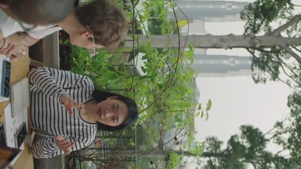 Vertikální záběr mladé asijské podnikatelky komunikující s týmem spolupracovníků během neformálního setkání na venkovní terase - Záběry, video