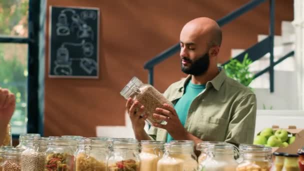 Koopman toont kruiden en voedingsmiddelen in containers of potten aan veganistische klant terwijl hij boodschappen doet. Consumenten uit het Midden-Oosten willen biologische, natuurlijke producten kopen. - Video