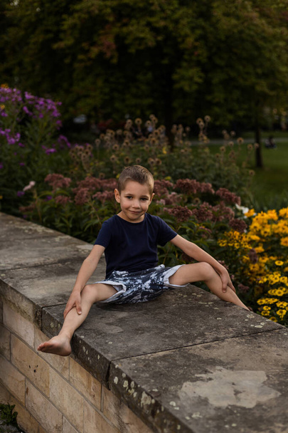 Ένα αγόρι παίζει κοντά σε λουλούδια στο πάρκο. Παιδική διασκέδαση κατά τις καλοκαιρινές διακοπές. Υψηλής ποιότητας φωτογραφία - Φωτογραφία, εικόνα