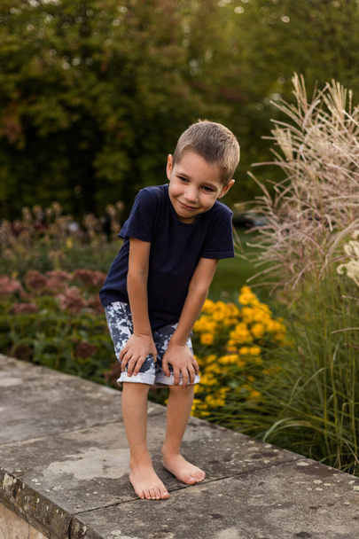 Egy fiú a virágok közelében játszik a parkban. Gyermek szórakozás a nyári szünetben. Kiváló minőségű fénykép - Fotó, kép