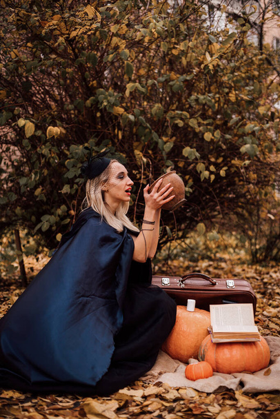 Una joven bruja en el bosque hace un hechizo, lee un libro. Magia en el bosque. Halloween. Foto de alta calidad - Foto, imagen