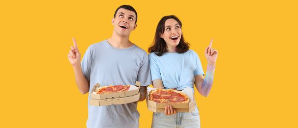 Heureux jeune couple avec de délicieuses pizzas pointant quelque chose sur fond jaune - Photo, image