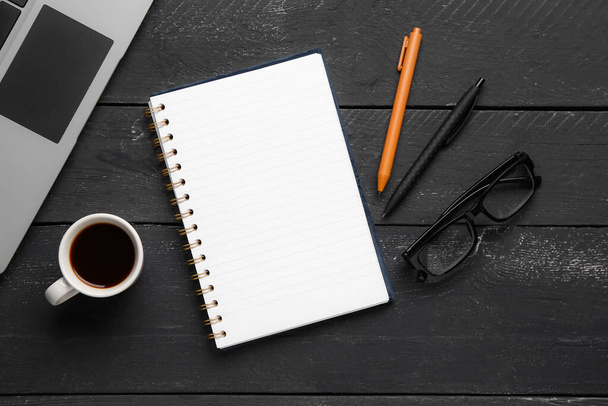 Caderno com óculos e xícara de café saboroso em fundo de madeira preta - Foto, Imagem