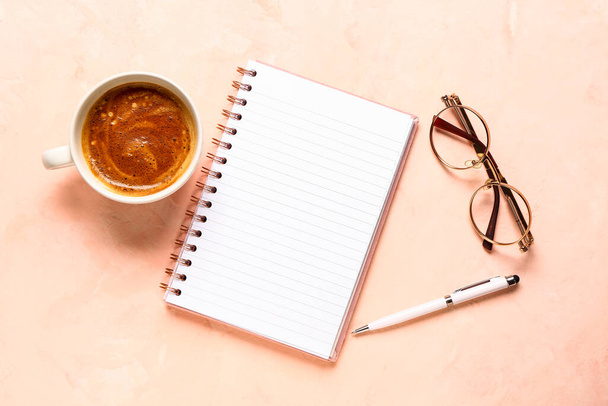 Notebook with eyeglasses and cup of tasty coffee on pink background - Photo, Image
