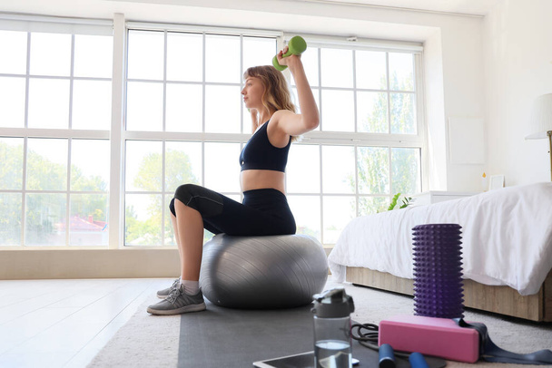 Молода спортивна жінка тренується з фітнес-кулькою і гантелі вдома - Фото, зображення