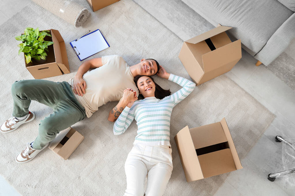 Happy young couple holding hands in room on moving day, top view - Photo, Image