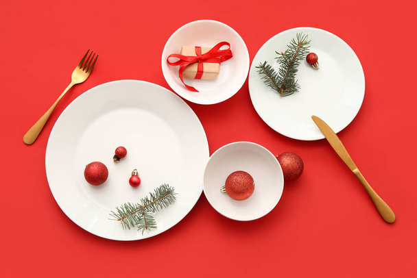Красивая сервировка стола с рождественскими шарами, елками и подарочной коробкой на красном фоне - Фото, изображение