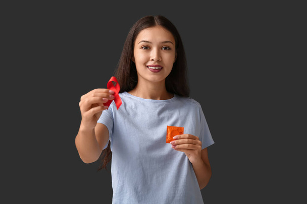 Досить молода жінка з червоною стрічкою і презервативом на чорному тлі. Всесвітній день боротьби зі СНІДом - Фото, зображення