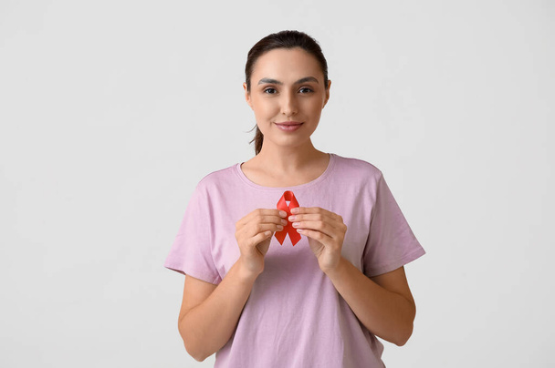 Νεαρή γυναίκα με κόκκινη κορδέλα σε λευκό φόντο. Έννοια της ενίσχυσης - Φωτογραφία, εικόνα