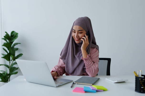 Müslüman kadın çalışan. Ofisteki müşterilerle konuşmak için telefonu kullanıyor. - Fotoğraf, Görsel