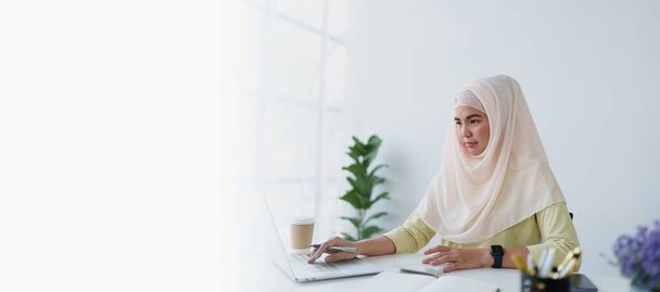 ムスリムの女性は,仕事で自分のアカウントをチェックするために計算機,コンピュータ,ラップトップを使用します. - 写真・画像