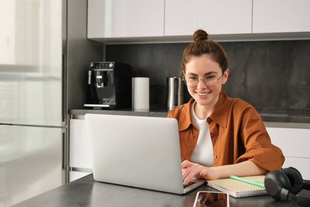 Evden çalışan genç bir kadının portresi. Mutfakta dizüstü bilgisayar kullanarak iş yeri kuruyor. Bilgisayar ödevi yapan öğrenci. - Fotoğraf, Görsel