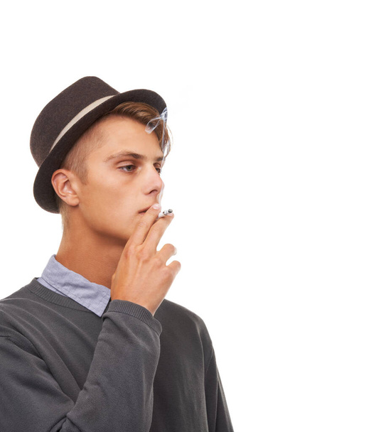 Młody człowiek, kapelusz i palenie papierosów w stylowy sposób odizolowane na białym tle studio. Fajny mężczyzna, model lub palacz schładzający się w zabytkowej odzieży lub mający przypadkowy dym na makiecie. - Zdjęcie, obraz