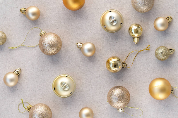 Αισθητικό κομψό εορταστικό μοτίβο με χρυσό παστέλ Χριστούγεννα, Πρωτοχρονιάτικες μπάλες διακόσμησης, στολίδια σε ουδέτερο μπεζ λινό ύφασμα φόντο. - Φωτογραφία, εικόνα