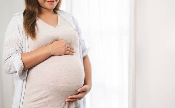 close-up de uma bela jovem durante o terceiro trimestre da gravidez Mulher grávida com braços na barriga redonda, sorrindo, relaxar expressão.. - Foto, Imagem